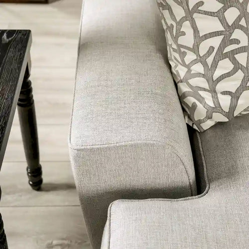 Un canapé rembourré en tissu gris clair avec un style de transition aux tons bleus, orné de rivets et doté de coussins.